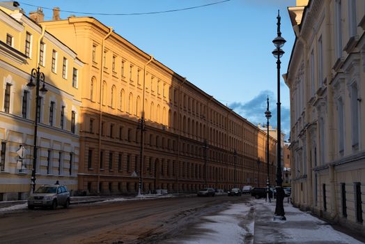 Snow-covered city street with classic architecture illuminated by golden sunlight.