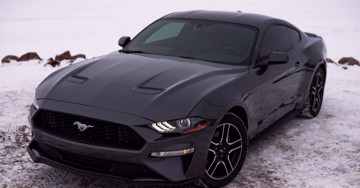 A sleek black Ford Mustang sports car parked on a snow-covered road in winter setting.