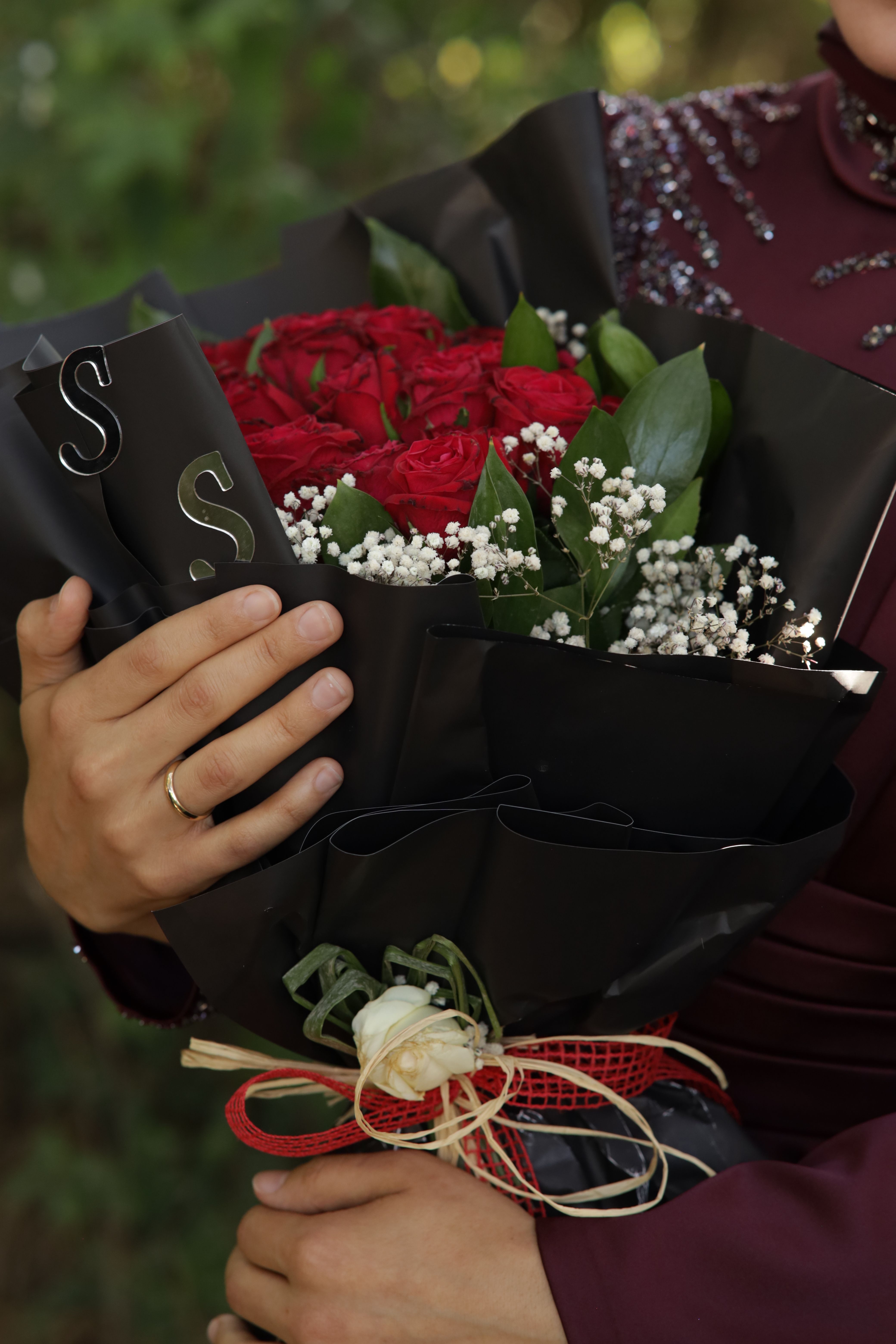 A close-up shot of a red rose bouquet held by hands in an outdoor setting.
