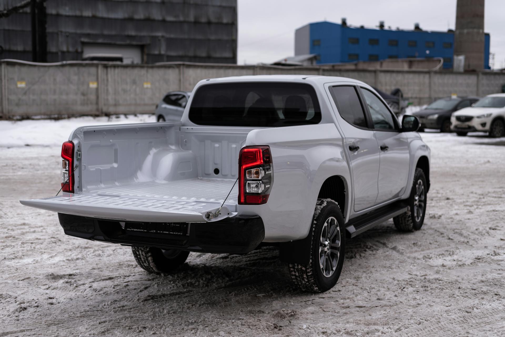 White pickup truck parked in a snowy industrial area, showcasing its open cargo bed.
