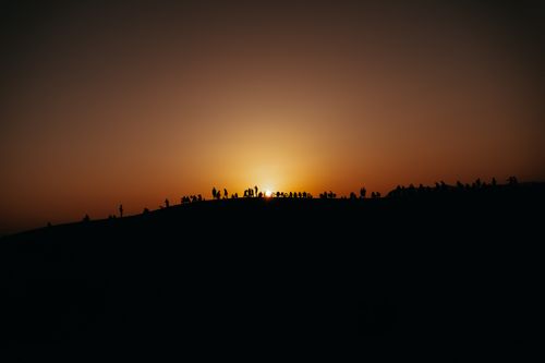 Free Silhouetted group of people on a ridge watching a sunset, creating a serene travel scene. Stock Photo