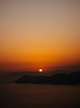 Stunning view of a sunset casting warm hues over mountains and calm sea.