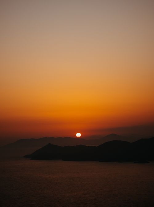 Free Stunning view of a sunset casting warm hues over mountains and calm sea. Stock Photo