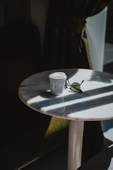 A disposable coffee cup and sunglasses on a sunlit table in Ankara, Türkiye.