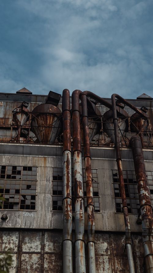 Free An abandoned industrial building with rusty pipes and a cloudy sky. Stock Photo