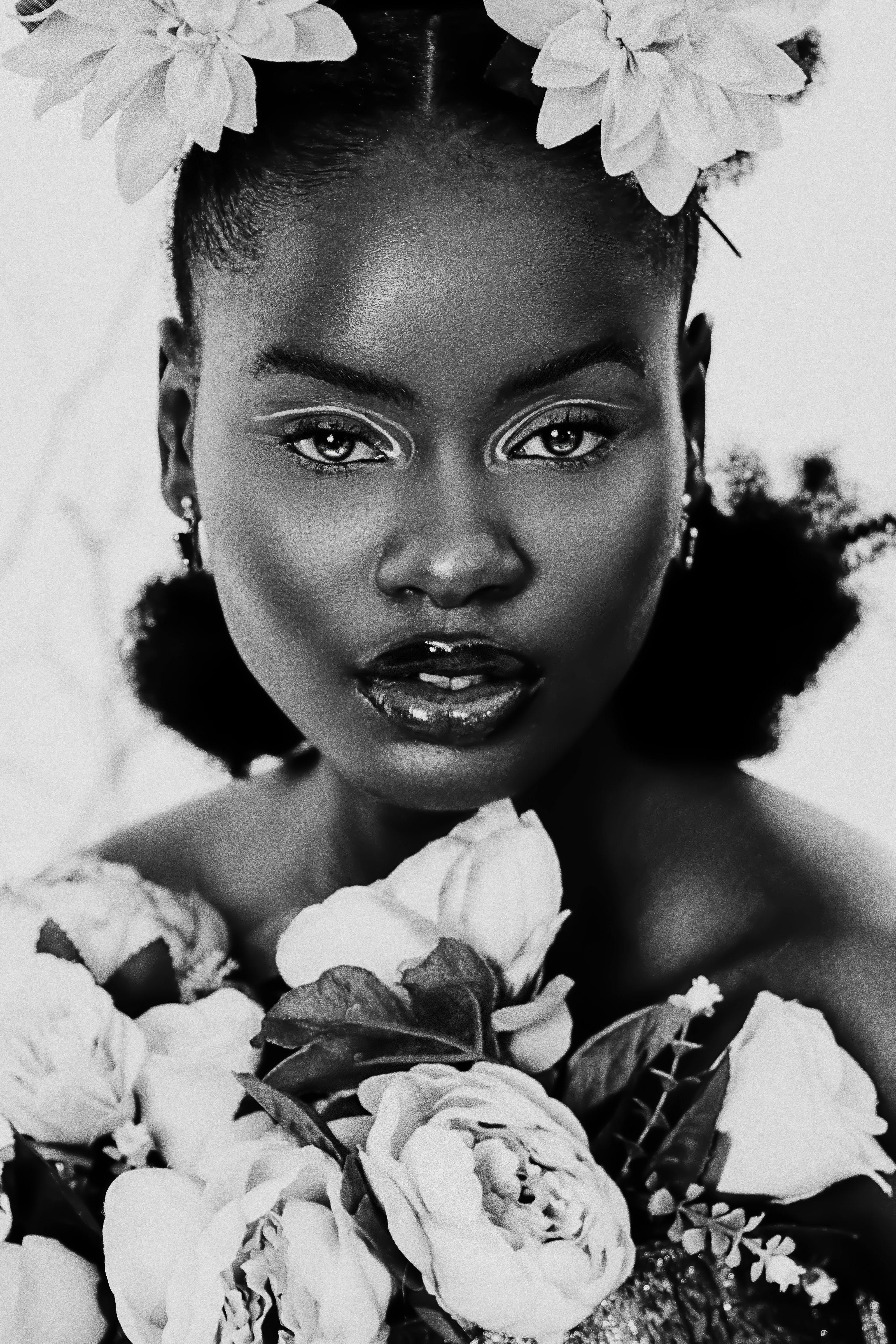 Stunning black and white portrait of an African woman adorned with flowers, captured in a studio setting.