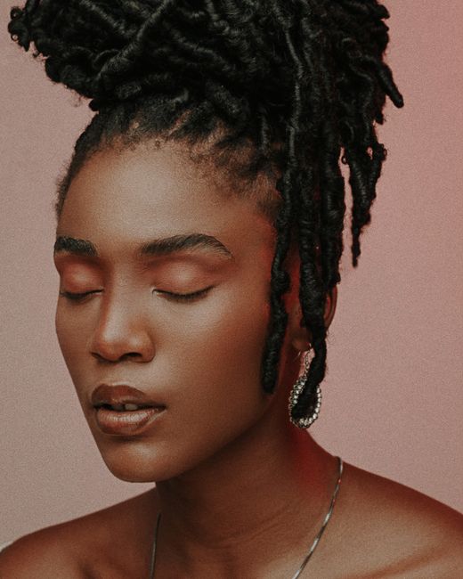 Serene portrait of a woman with closed eyes and stylish dreadlocks against a soft background.