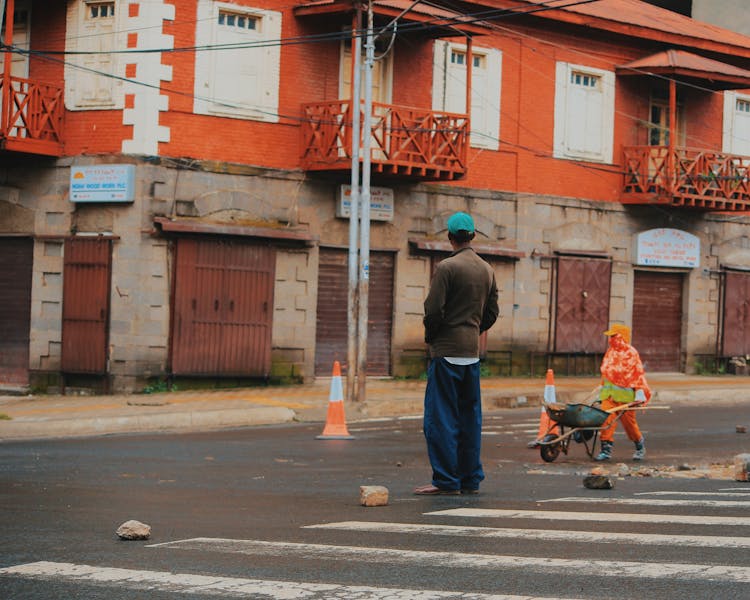 People On A Street Near An Old Red House With Balconies