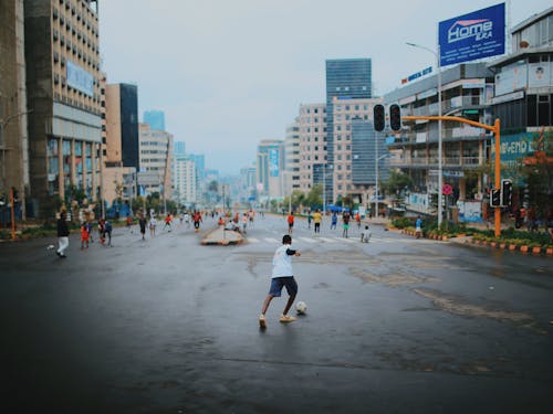 A Boy Kicking a Soccer Ball on the Street in City 