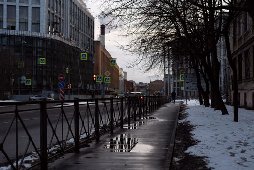 City street in winter with snow and reflections on wet sidewalk and street.