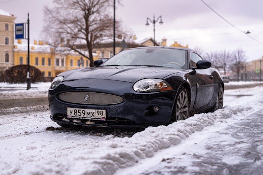 A sleek black luxury car parked on a snow-covered city street in winter.