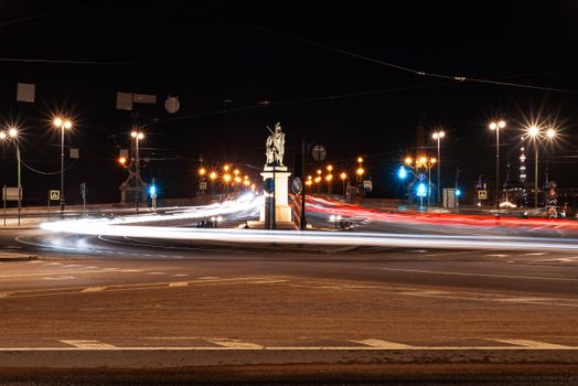 Long exposure of illuminated city streets at night, showcasing dynamic light trails around a central monument.