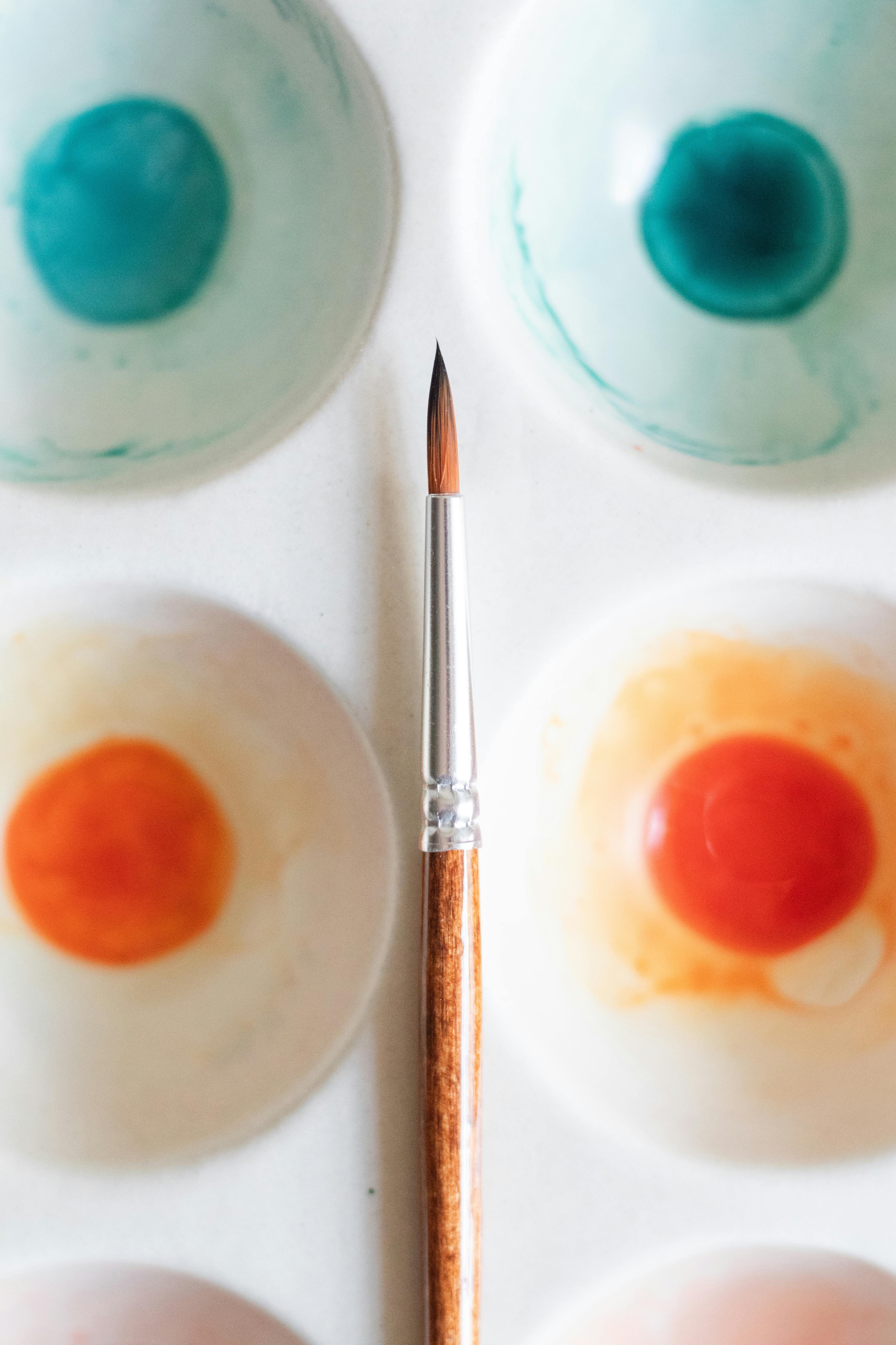 Close-up of a paintbrush with colorful acrylic paint palette for creative projects.