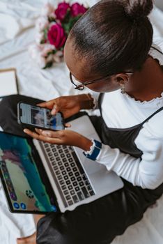 A young woman using a laptop and smartphone simultaneously indoors, illustrating modern connectivity and multitasking.