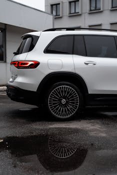 Sleek white Mercedes-Benz EQB SUV parked outdoors reflecting in a puddle.