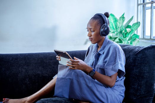 Woman working remotely from home on a tablet with headphones, sitting on a sofa.