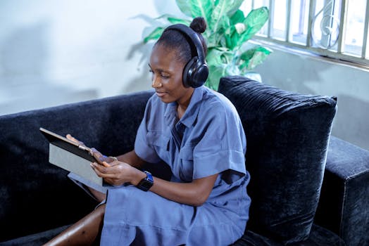 A woman using headphones and a tablet while working from home on a sofa.