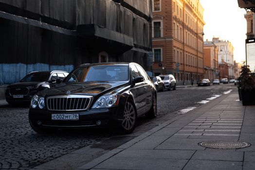 A luxurious black Maybach car parked on a cobblestone street in an urban setting at sunset.
