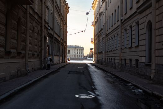 A narrow urban alleyway leading to a bright open area with historic architecture in winter.