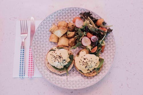 Plate of Eggs Benedict with Potatoes and Salad in a Table
