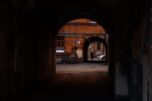 Free A moody view through a dark tunnel into a rustic urban courtyard with old buildings. Stock Photo