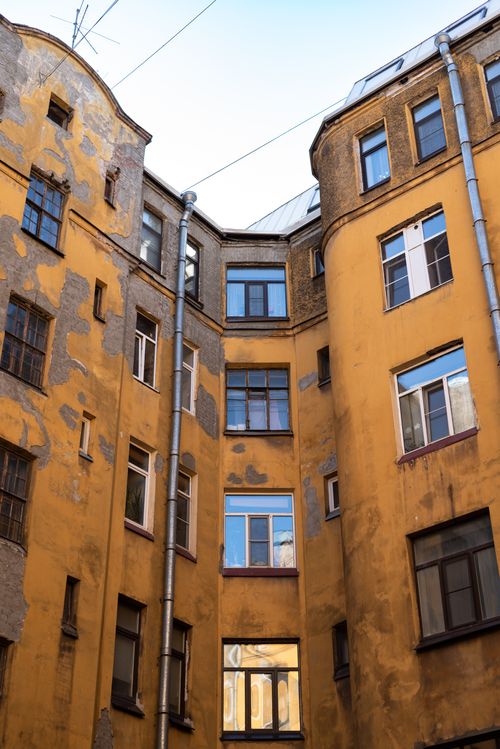 Free A worn and weathered urban courtyard showcasing aged yellow facades and windows. Stock Photo