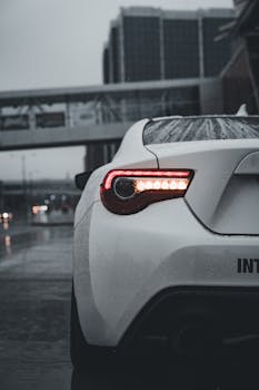 A sleek white sports car parked in a rainy urban setting, showcasing modern design and elegance.