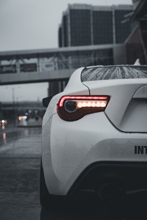 Free A sleek white sports car parked in a rainy urban setting, showcasing modern design and elegance. Stock Photo