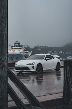 A sleek white sports car parked in a rainy urban harbor setting, showcasing modern design and style.