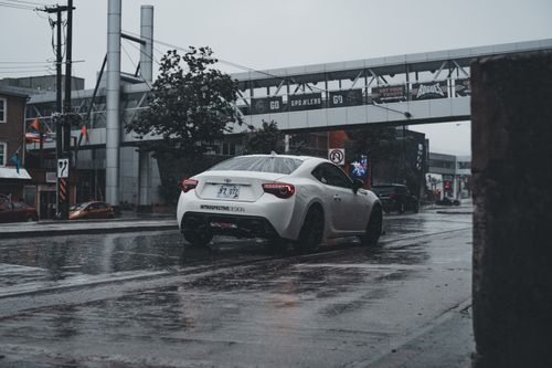 Free A white sports car on rainy city street captures urban vibe and motion. Stock Photo
