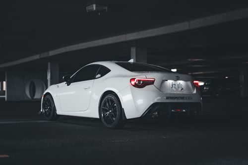 Free A sleek white Toyota sports car parked in a dimly lit urban parking garage, featuring rear street view. Stock Photo
