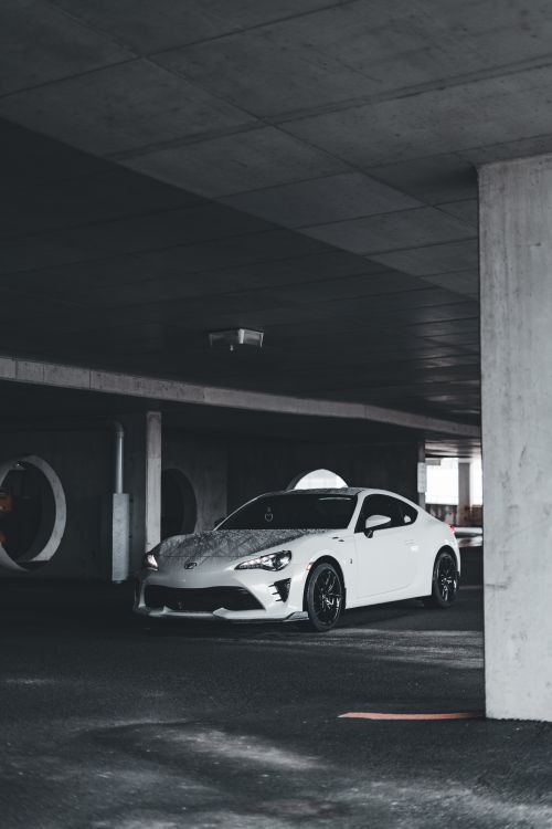 Free Sleek white sports car captured in a dimly lit urban underground parking garage. Stock Photo