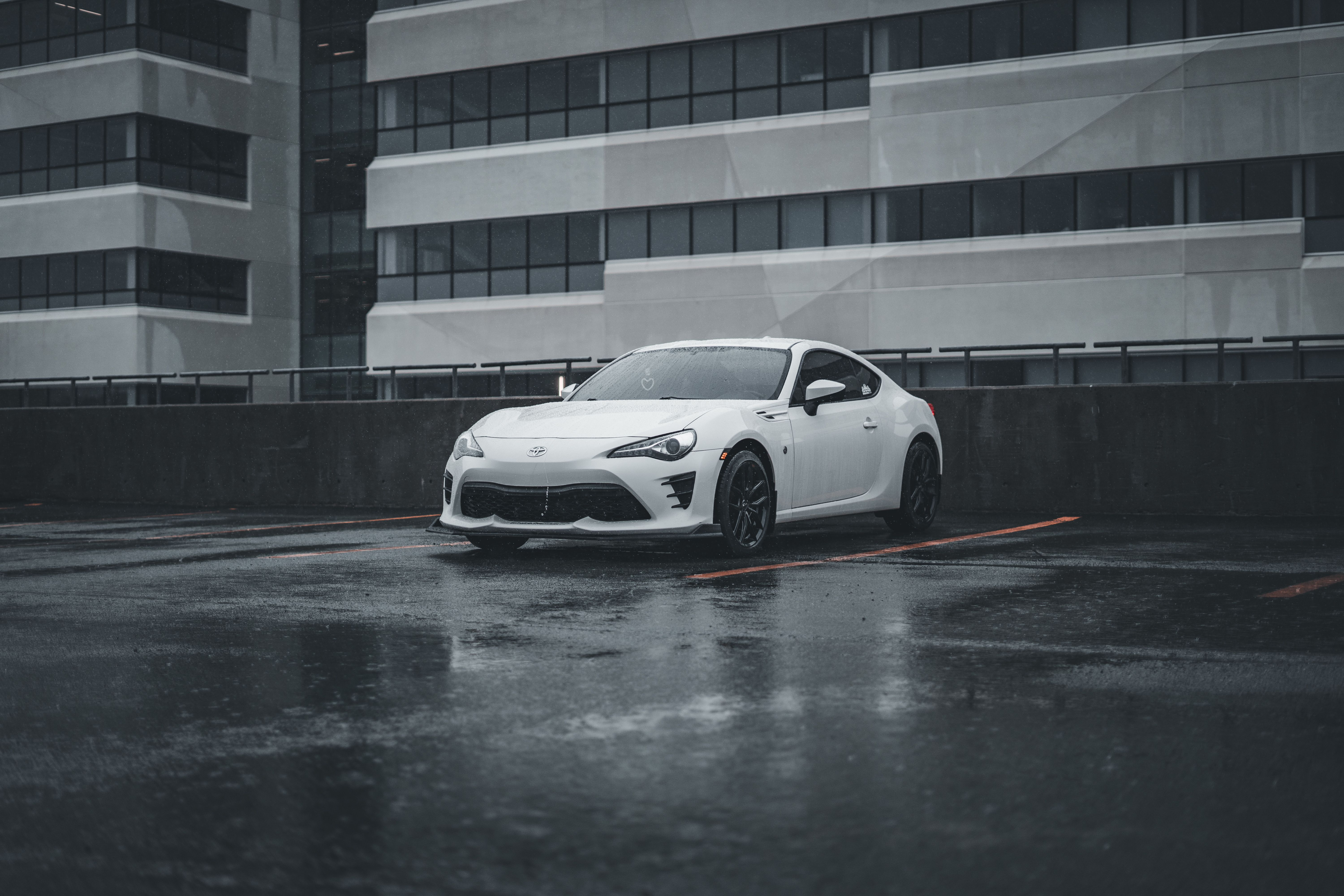A sleek white sports car parked in a rainy cityscape, showcasing modern urban architecture.