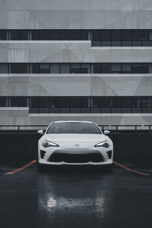 Free A stylish white sports car sits on a wet urban rooftop parking lot under overcast skies. Stock Photo