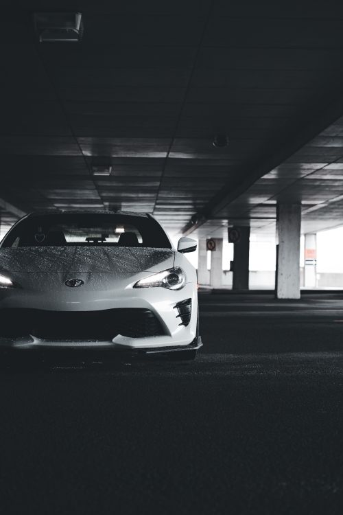 Free White sports car showcased in a dimly lit urban parking garage for a modern and dramatic effect. Stock Photo