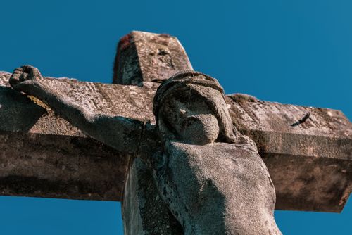 Free Close-up of a stone crucifix sculpture of Jesus Christ with a bright blue sky backdrop. Stock Photo