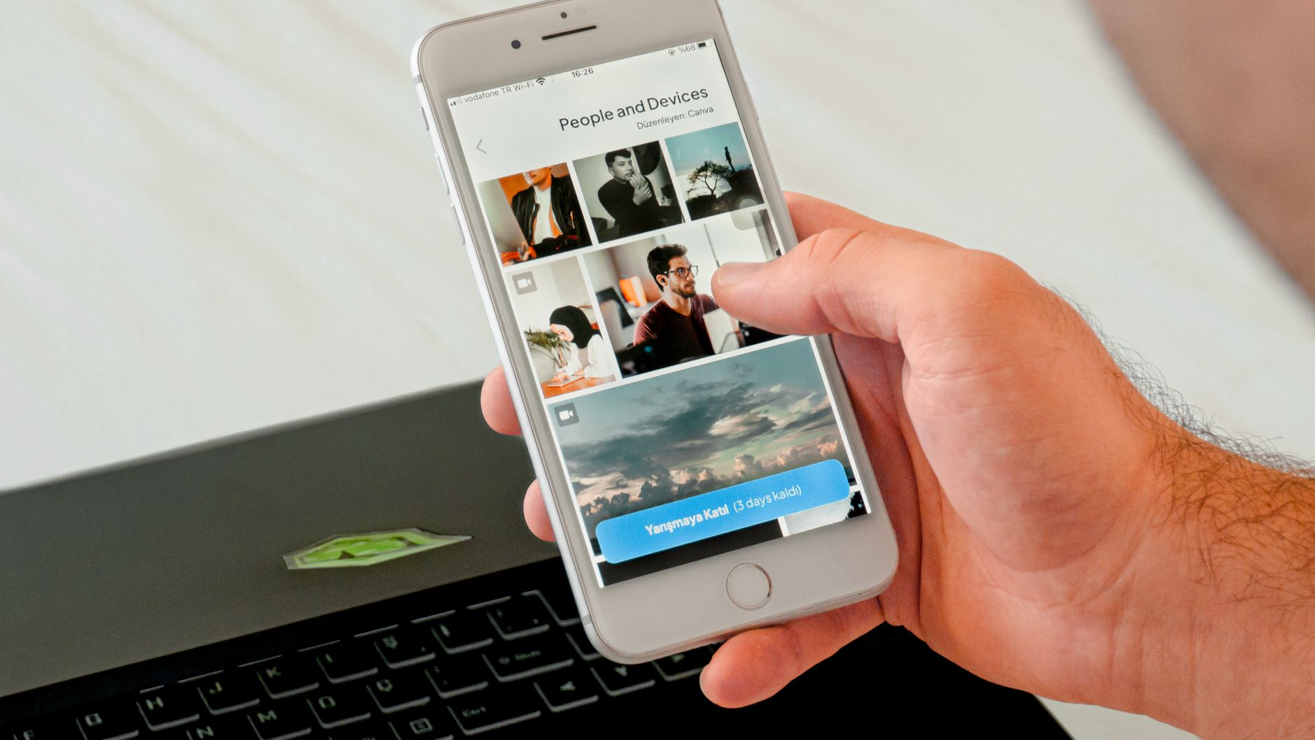 Close-up of a hand browsing photos on a smartphone with a laptop in the background, showcasing technology use.