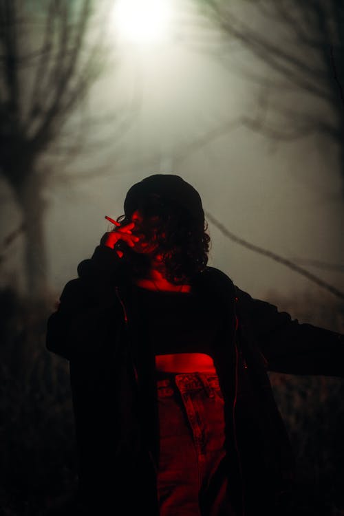 Person Illuminated by Red Light Smoking a Cigarette in the Forest at Night