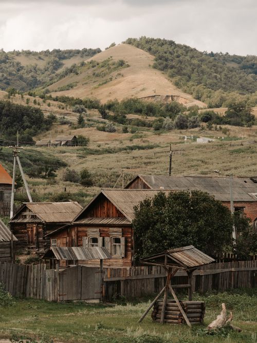 Free Rustic wooden houses nestled in a serene rural village landscape with hills. Perfect for travel and architecture enthusiasts. Stock Photo