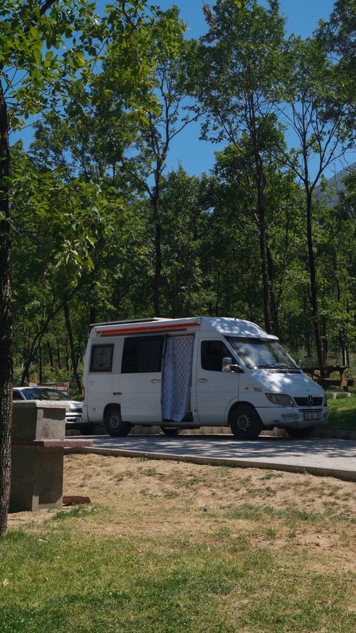 Free A white campervan parked in a lush green forest setting on a sunny day, perfect for camping trips. Stock Photo