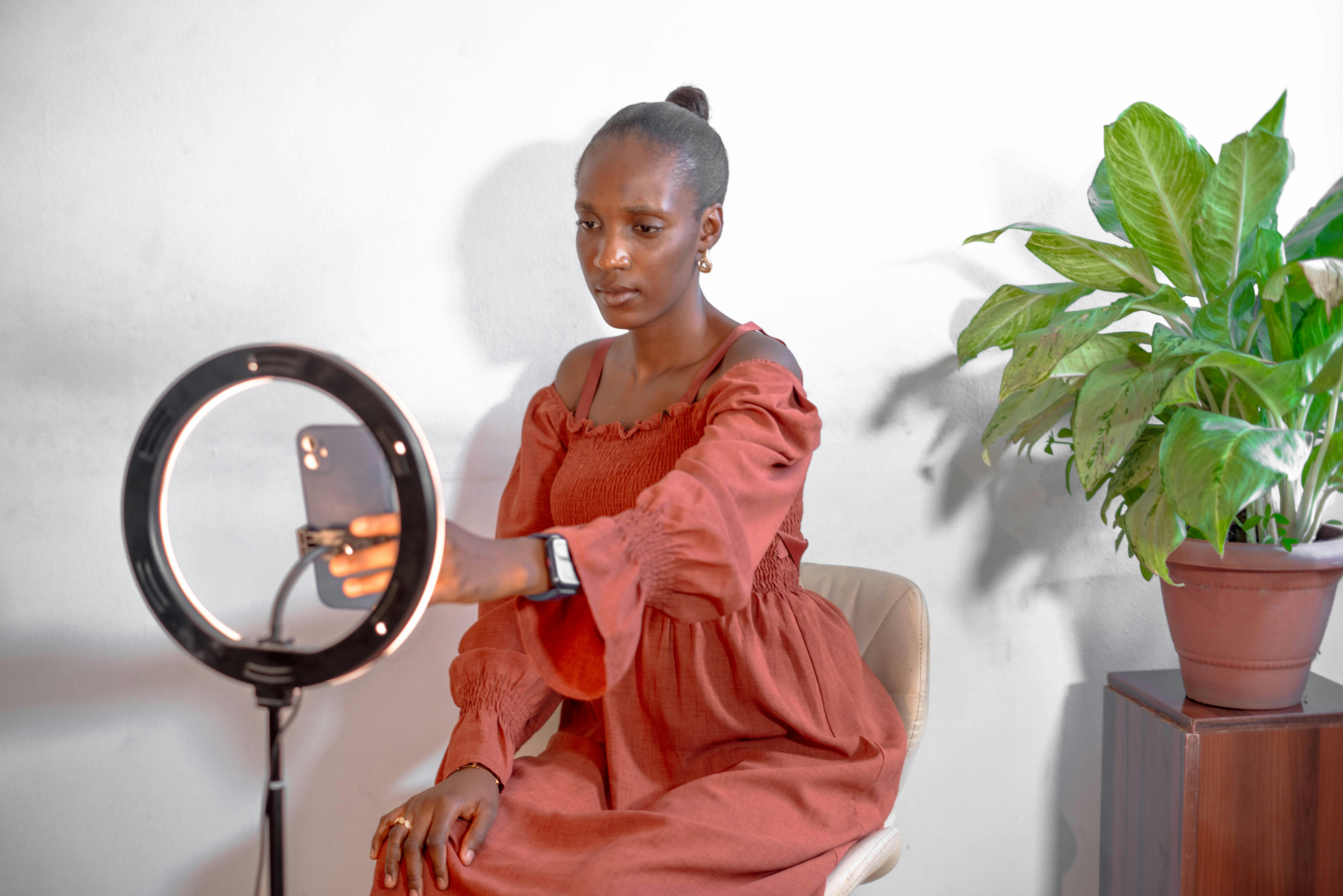 Free A young woman uses a smartphone and ring light for vlogging indoors. Stock Photo