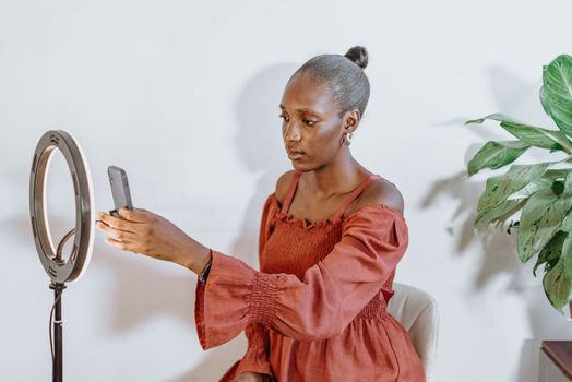 A young woman setting up her smartphone with a ring light indoors for video creation.