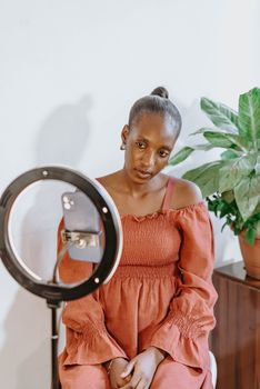 African woman using a ring light and phone for vlogging indoors.