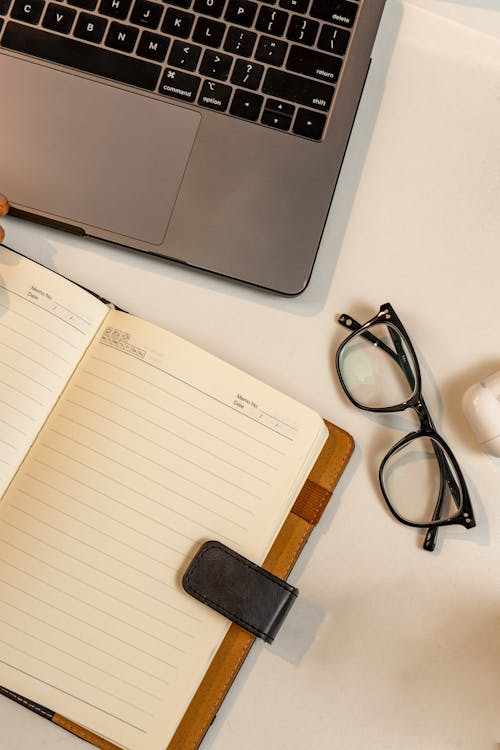 An Empty Notebook Lying next to a Laptop and Eyeglasses 