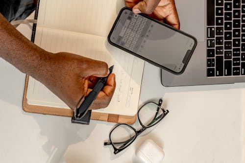 Top View of a Man Holding a Smartphone and Writing in a Notebook 