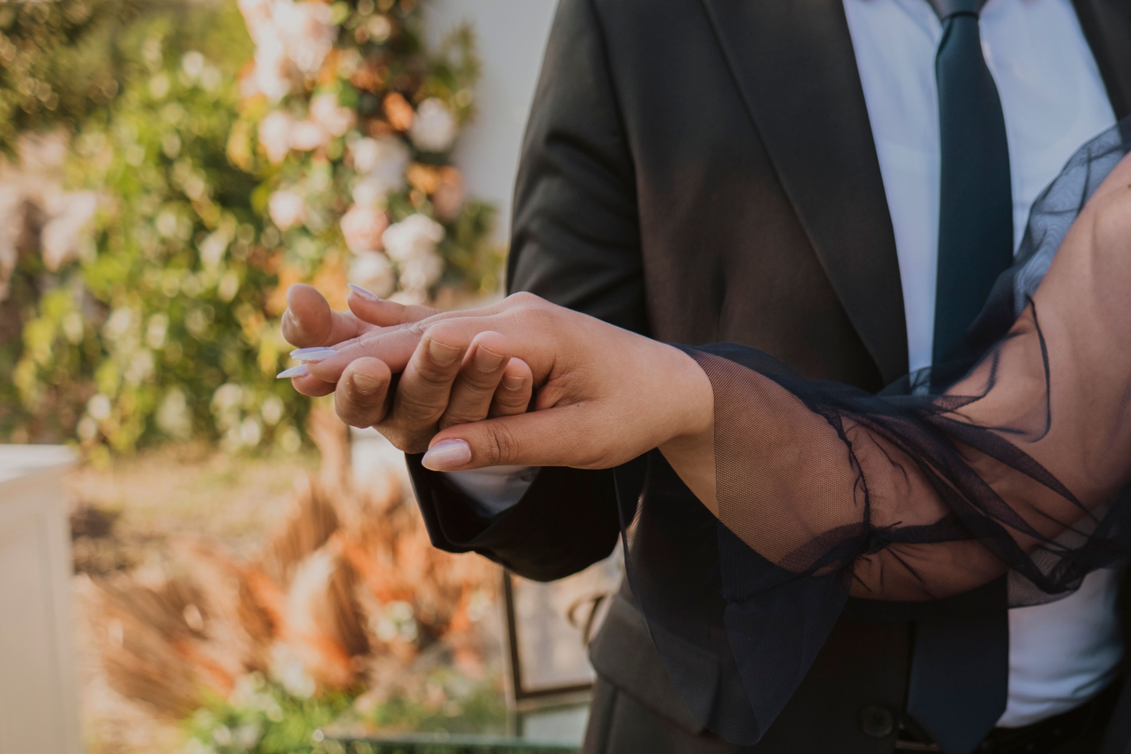 Close-up of a couple holding hands at a formal outdoor gathering, showcasing elegance and connection.