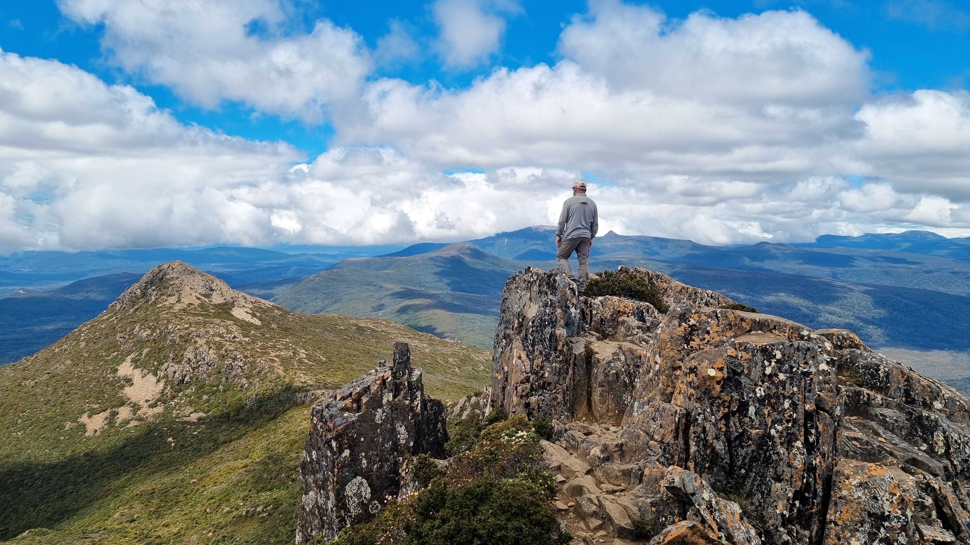 Man standing on rocky summit in Hartz Mountains, Tasmania, enjoying the panoramic landscape.