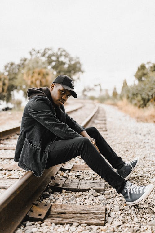 Young Man in a Black Outfit Sitting on the Railway 