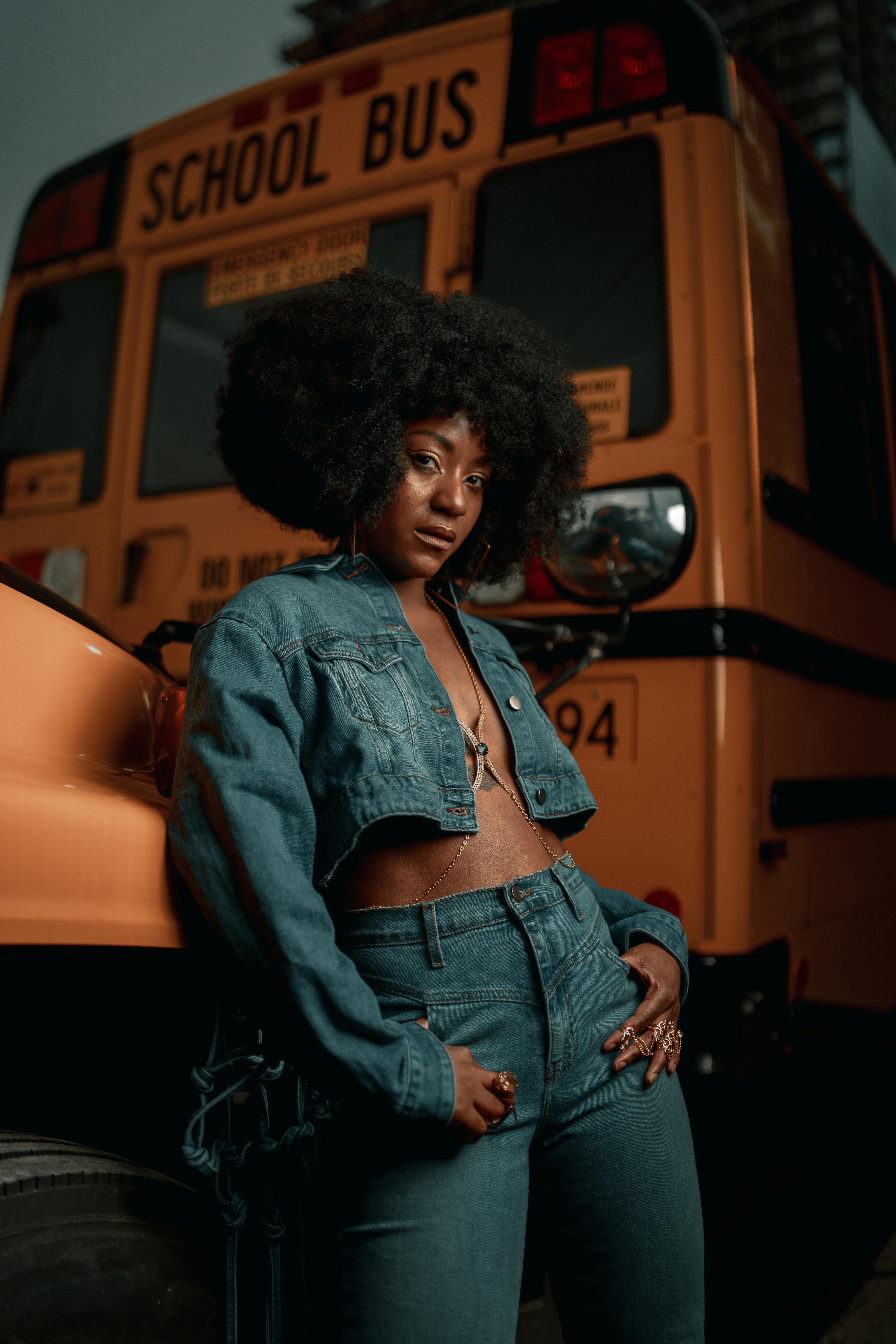 a woman in jeans and a jacket standing next to a school bus