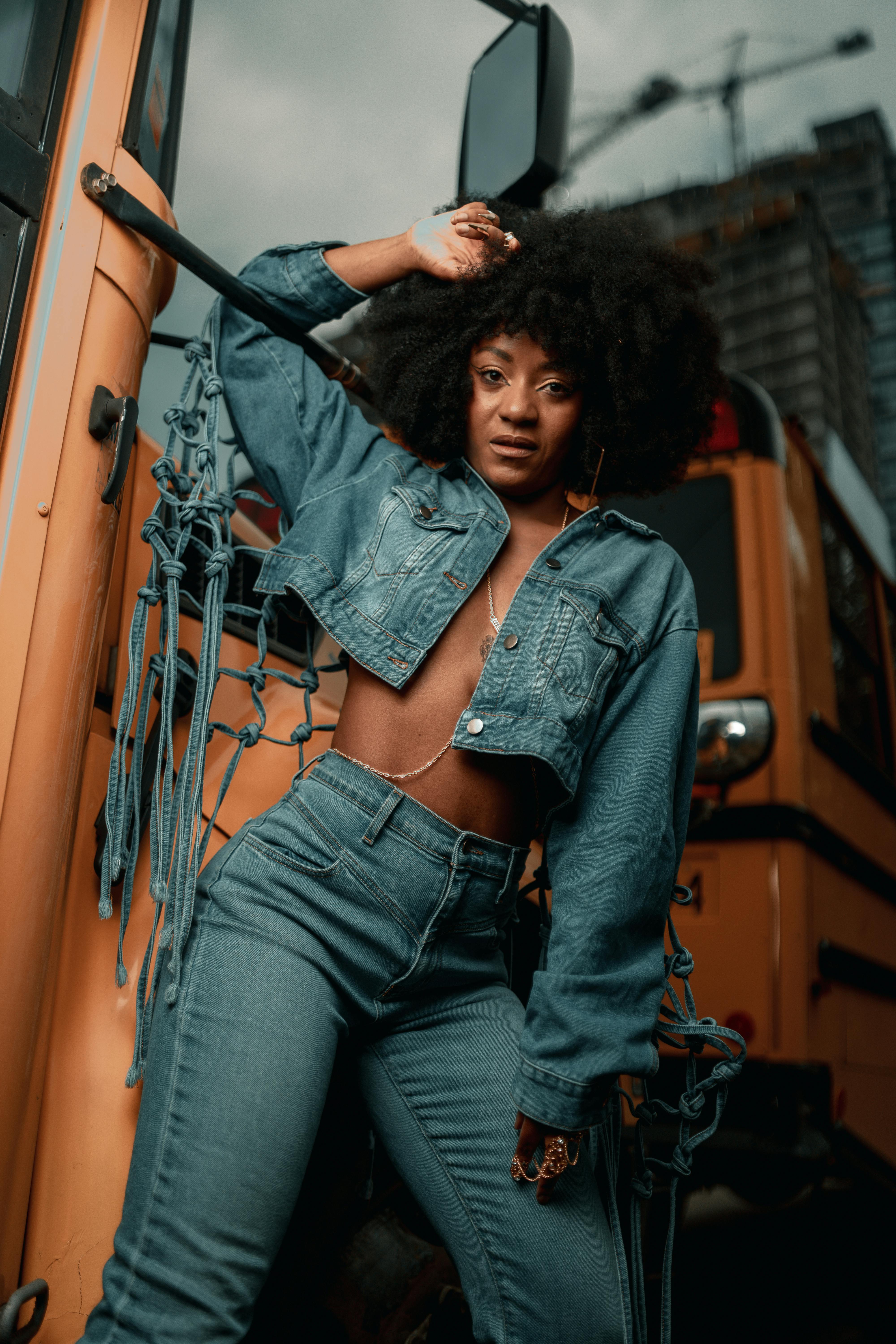 a woman in jeans and a denim jacket standing next to a school bus